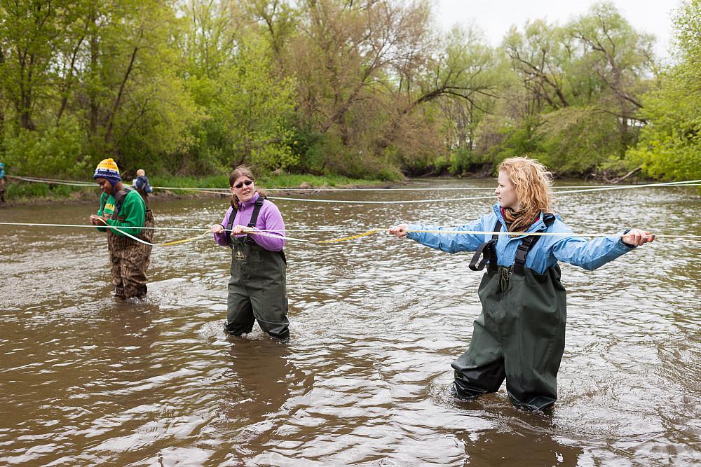 Three students test the water movement of a stream during their field study for a hydrogeology class.